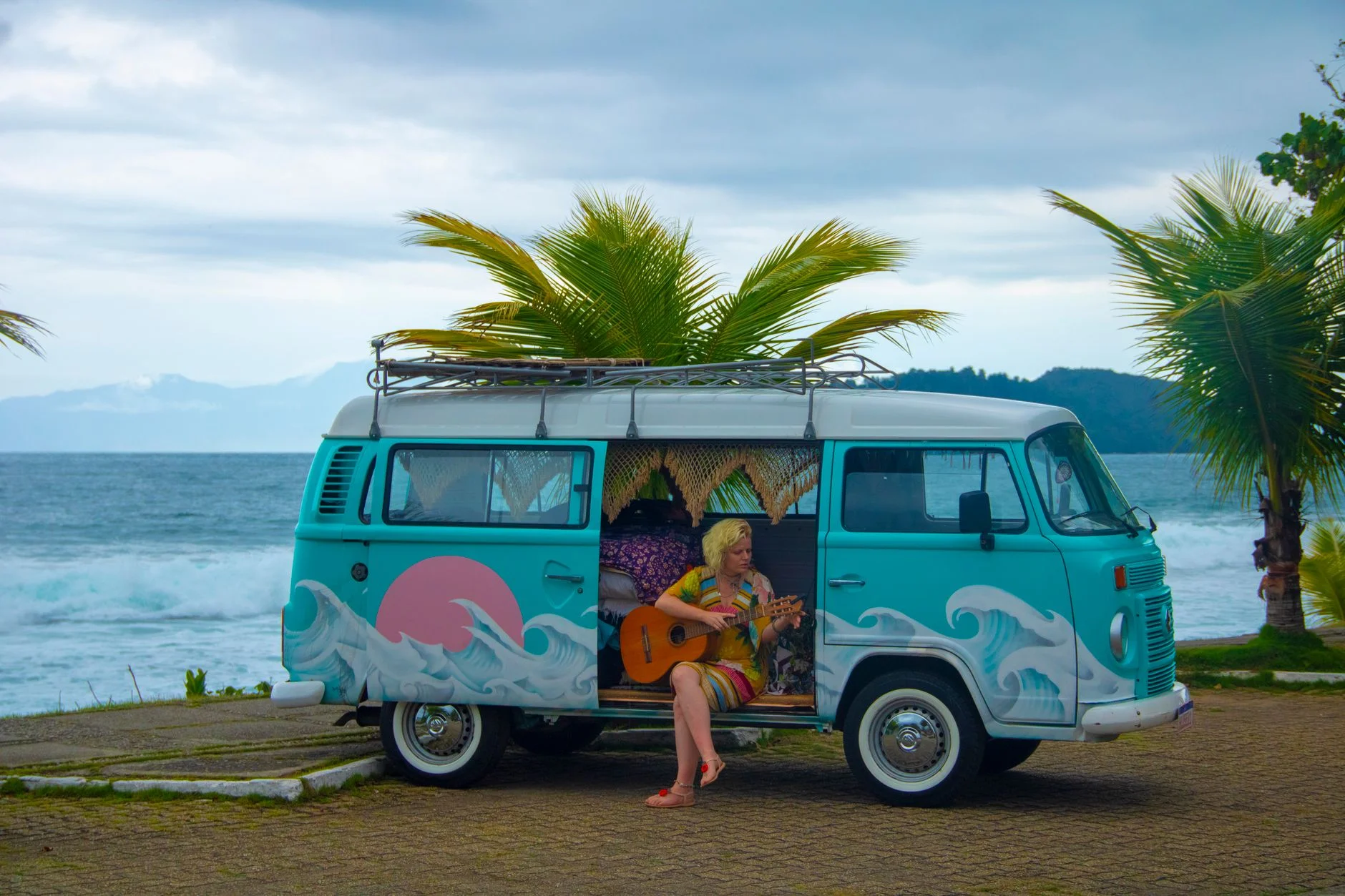 A photorealistic, professional photography, 8K image of two people, a traveler and a local host, sharing a laugh while cooking together in a rustic kitchen, warm evening light, sharp focus on their interaction, depth of field, shot on a high-end DSLR. Colorful camper van on a tropical beach with a woman playing guitar, ocean view. — Foto: Luiz Oliveira / Pexels