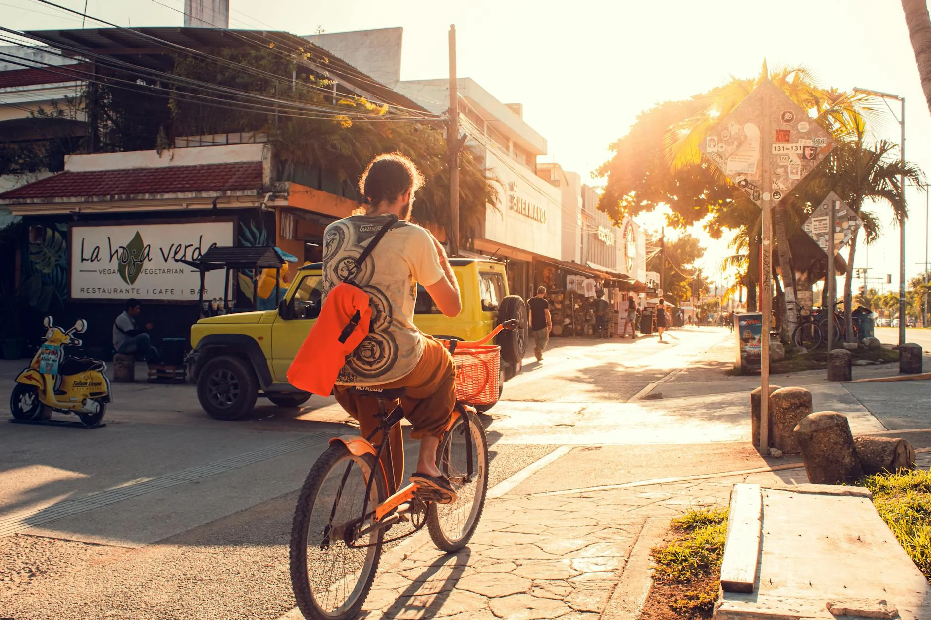 A photorealistic, professional photography, 8K, cinematic lighting, sharp focus, depth of field, shot on a high-end DSLR of a sleek, modern tram moving through a bustling, green urban landscape, with people waiting at a clean, well-designed tram stop. The scene conveys efficiency and environmental consciousness in city transport. A man cycling through a busy city street during sunset with a shoulder bag. — Foto: Isai Martinez / Pexels