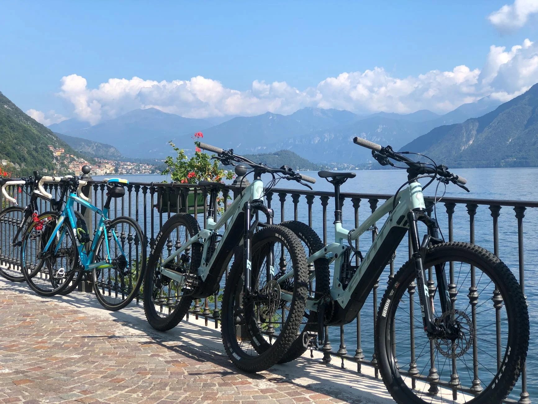 A photorealistic, professional photography, 8K, cinematic lighting, sharp focus, depth of field, shot on a high-end DSLR of a modern, electric taxi pulling up to a picturesque canal in Amsterdam, with bicycles parked neatly along the bridge and a historical building in the background, symbolizing sustainable urban travel options. Bicycles lined up by a scenic view of Lake Como and surrounding mountains under a clear blue sky. — Foto: Tosca Greco / Pexels