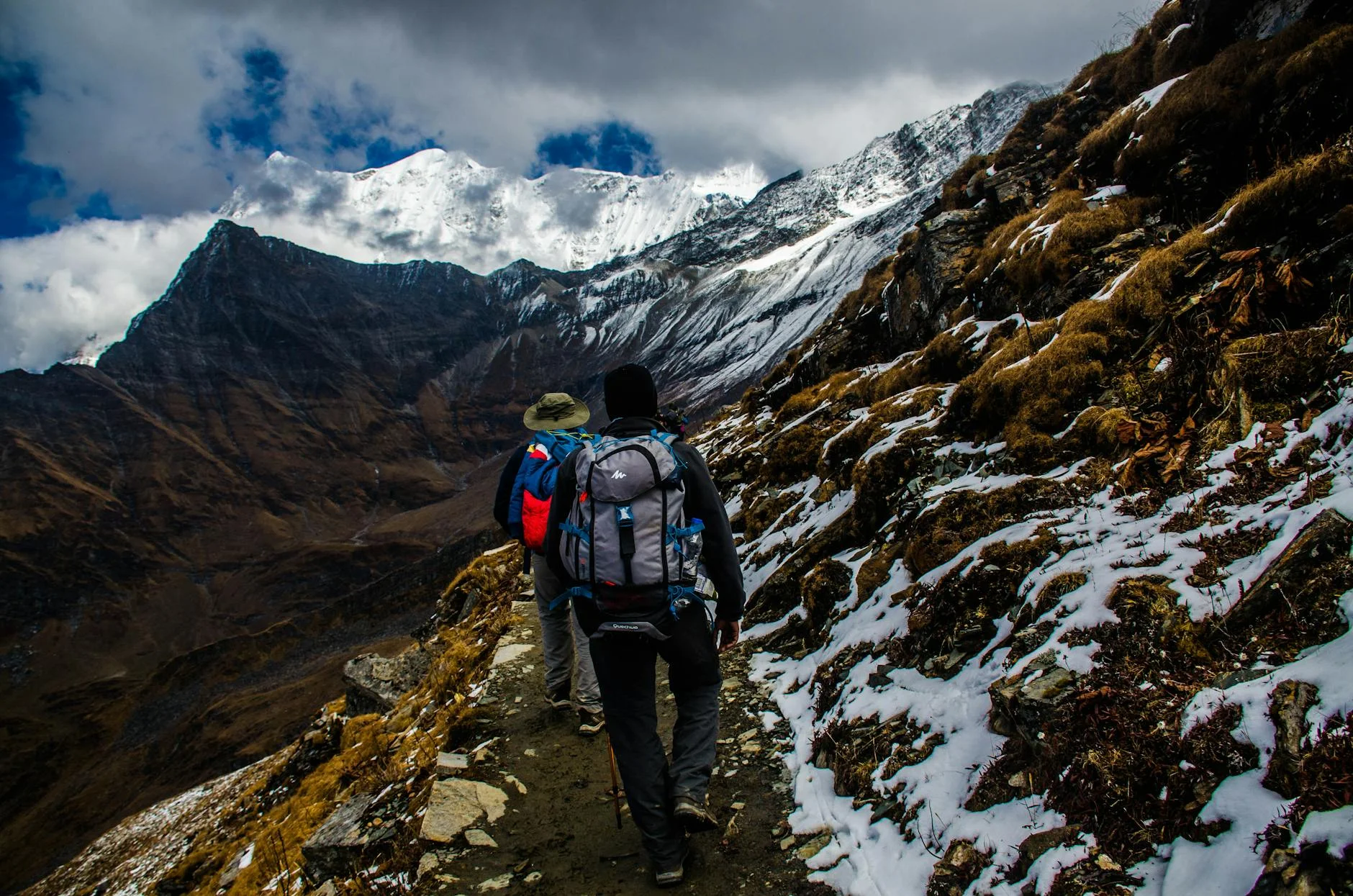 Two hikers navigating a snowy trail in rugged mountainous terrain under dramatic skies. — Foto: Saikat Ghosh / Pexels